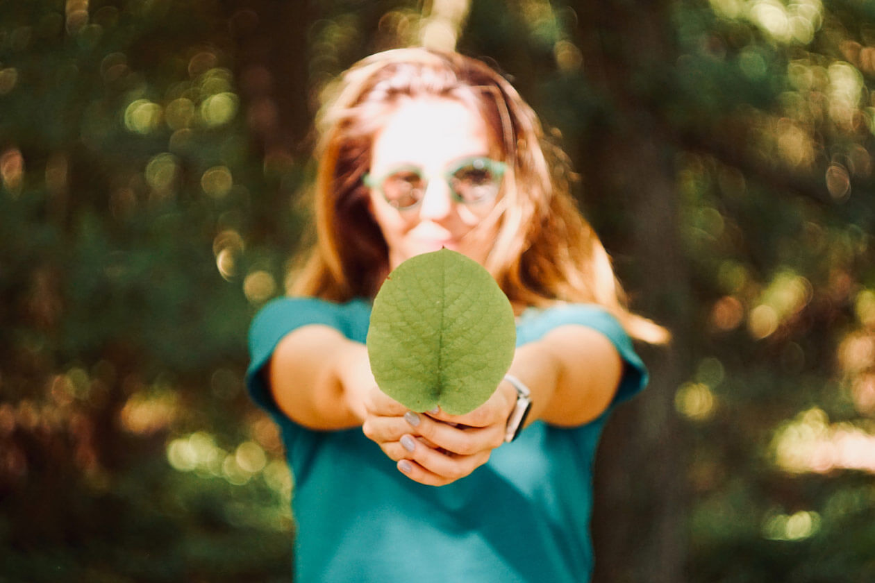 Young woman holding a green leaf forward with blurred forest background